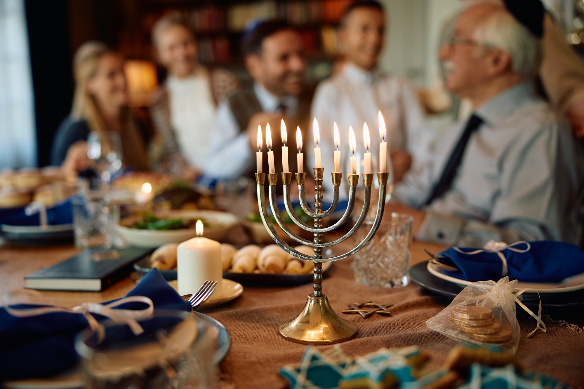 Lit candles in menorah with Jewish multigeneration family gathered for Hanukkah celebration.