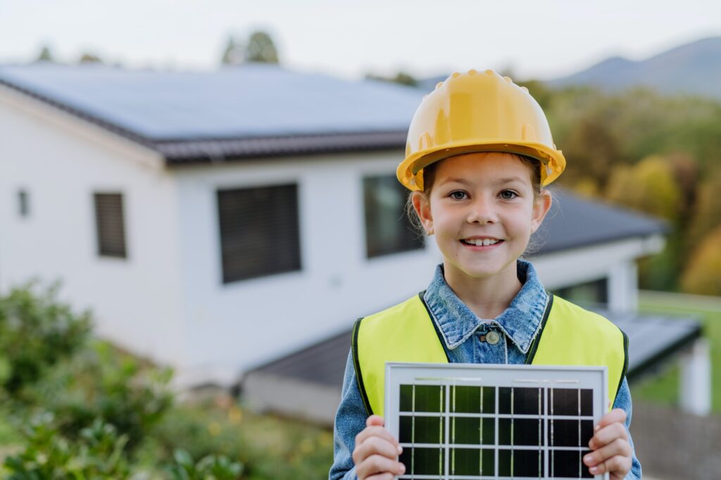 Little girl with protective helmet and reflective vest holding photovoltaics solar panel