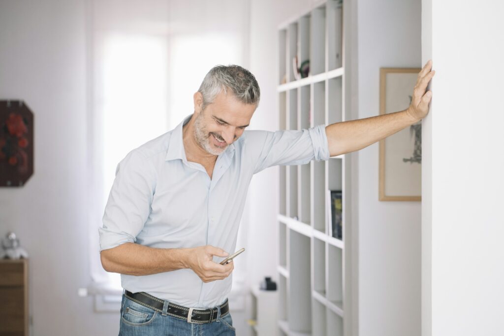 Smiling mature man using cell phone at home